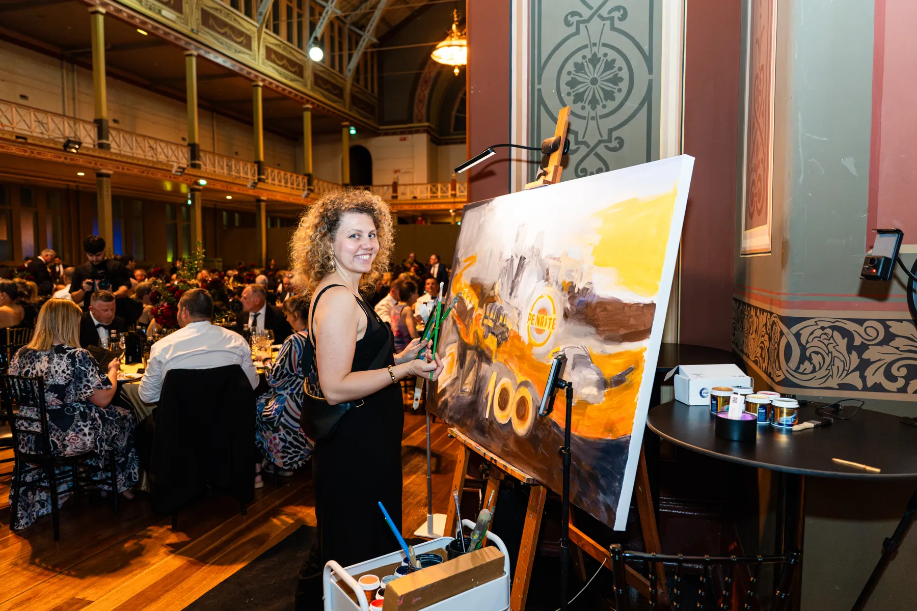 Olga smiling towards the camera beside her painting at the Penrite centenary gala